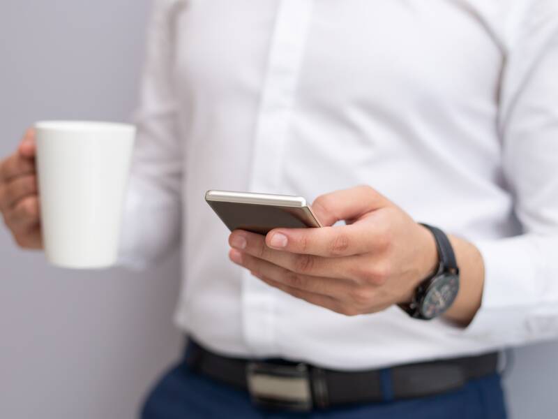 Mann mit Kaffeetasse und Smartphone in den Händen.