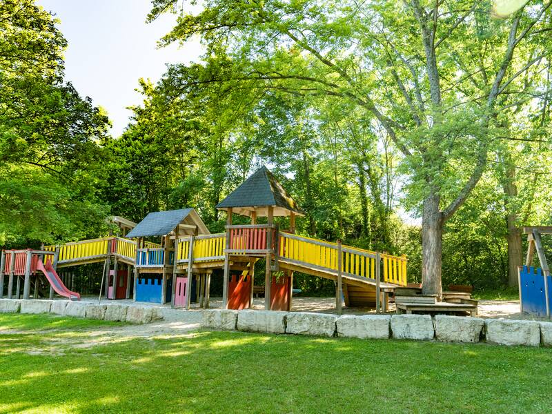 Dieses Bild vom Sportbad Heitersheim zeigt den großen Spielplatz im Schatten der Bäume.